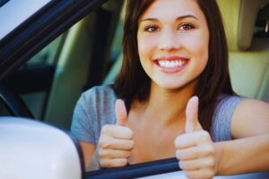 Ragazza sorridente mostra i pollici in su dal finestrino dell'auto