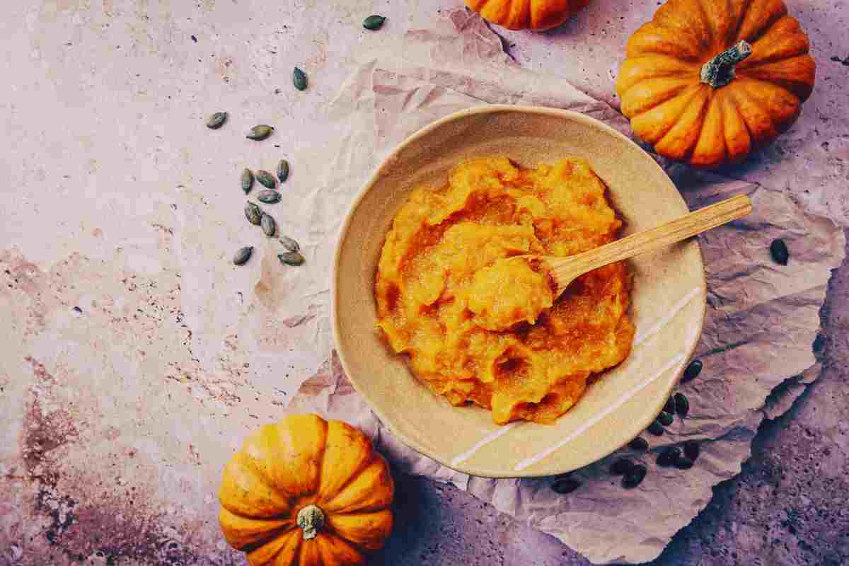Scodella ripiena di crema di zucca accanto a zucche intere e semi